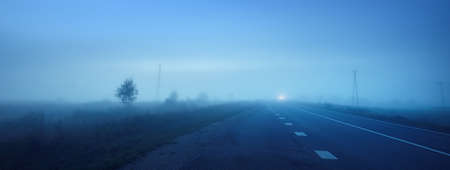Panoramic view of the empty highway through the fields in a fog at night. Moonlight, clear sky. Sunrise. Europe. Transportation, logistics, travel, road trip, freedom, driving. Rural sceneの写真素材