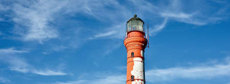 And old red lighthouse against clear blue sky with cirrus clouds. Baltic sea shore, Paldiski. Summer...