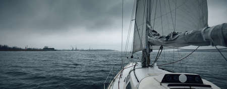Yacht sailing in a thunderstorm on a rainy autumn day. Top down view from the deck to the bow, mast and sails. Dramatic stormy sky, dark clouds. Norwayの写真素材