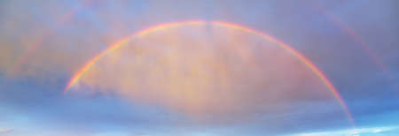 Dramatic sunset sky with double rainbow and colorful glowing clouds after the rain. Epic cloudscape. Fickle weather. Cyclone, storm, meteorology, ecology, natureの写真素材