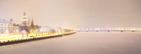 Panoramic aerial view of the illuminated snow-covered Riga old town and Daugava river from the...