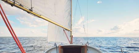 White sloop rigged yacht sailing at sunset. Clear sky after the storm. View from the deck to the...