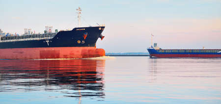 Large cargo ship sailing in the Baltic sea at sunset. Soft golden sunlight. Concept seascape. Panoramic view from the sailing boat. Freight transportation, nautical vessel, logisticsの写真素材