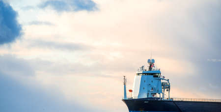 Large cargo ship sailing in the Baltic sea at sunset. Soft golden sunlight. Concept seascape. Panoramic view from the sailing boat. Freight transportation, nautical vessel, logisticsの写真素材