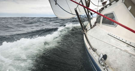 Yacht sailing during a thunderstorm on a rainy day. Close-up view from the deck to the bow, mast,...