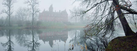 Pond and a castle in a forest park. Jaunmoku pils, Latvia. Fog. Atmospheric autumn landscape. Silence, loneliness, melancholy concepts. Panoramic viewの写真素材