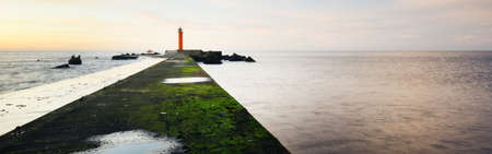 An empty promenade to the orange lighthouse with solar battery against colorful sunset sky. Stunning...