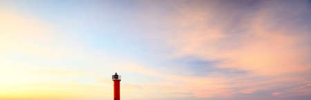 Orange lighthouse with solar battery against colorful sunset sky. Stunning cloudscape. Environmental conservation theme. Baltic sea, Riga bay, Latviaの写真素材
