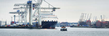 Large cargo ship unloading in Hamburg port terminal, Germany. Freight transportation, global communications, logistics, environmental damage themeの写真素材