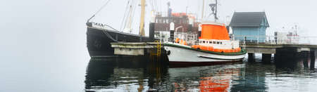 Small ships, yachts, sailing and fishing boats moored to a pier, in a thick white morning fog, close-up. Kiel, Germany. Transportation, logistics, industry, cityscape. Panoramic imageの写真素材