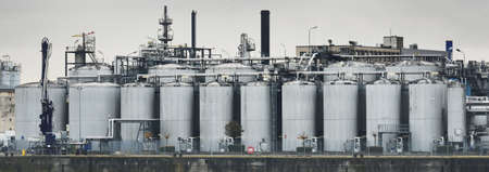 Chemical factory on a hazy day; silos, factory pipe, smoke. Dark panoramic urban cityscape. Industry, business, technology. fuel and power generation, ecological issues, environmental damageの写真素材