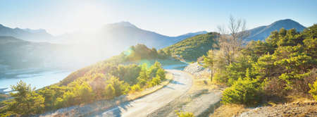 Winding asphalt road (highway) in the french Alps near lake Lac de Serre-Poncon on a clear sunny day. Panoramic landscape. Road trip in France, Europe. Travel destinations, nature, vacations, tourismの写真素材