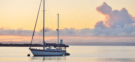 A two-masted sailboat (ketch) with a motorboat anchored on mooring near the shore of Craighouse at...
