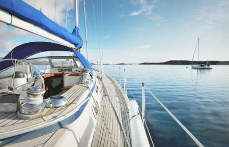 Sloop rigged modern yacht with wooden teak deck sailing near the shore of Jura island on a sunny...
