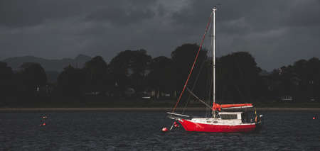Small red sailboat anchored on mooring near the shores of Firth of Clyde. Rhu, Scotland, UK....
