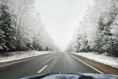 Empty highway (asphalt road) through the snow-covered forest, rural area. View from the car. Europe....