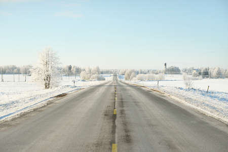 Empty highway (asphalt road) through the snow-covered forest and fields, rural area. Snow drifts....