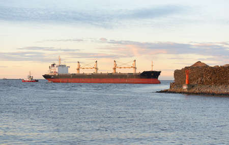 Large cargo ship arriving in port at sunset. Baltic sea.  Freight transportation, nautical vessel, global communications, logistics, shipping, delivery, industry, commerce, economyの写真素材
