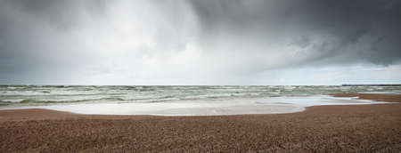 Sandy shore of the Baltic sea under the dramatic clouds after thunderstorm. Ventspils, Latvia. Epic seascape. Cyclone, gale, storm, rough weather, meteorology, climate change, natural phenomenonの写真素材