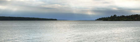 Rocky lakeshore and evergreen forest at sunset. Dramatic sky. BjÃ¶rkÃ¶ island, lake MÃ¤laren, Sweden. Pure nature, environmental conservation, ecotourism, vacations, sailing. Panoramic viewの写真素材