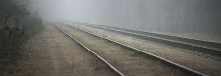 Railroad track in a thick white fog, forest in the background. Concept landscape. Freight and passenger transportation, industry, business, communications, environmental damage. Monochrome, mysteryの写真素材