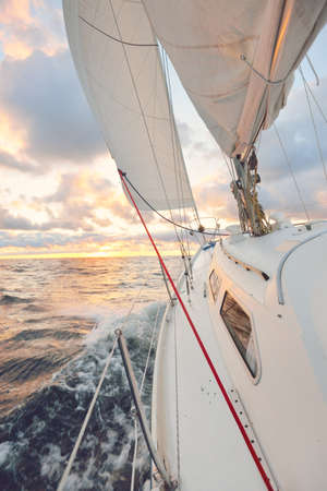 Yacht sailing in an open sea at sunset. Close-up view of the deck, mast and sails. Clear sky after...