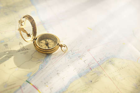 Retro style antique golden compass (sundial) and old nautical chart close-up. Vintage still life. Sailing accessories. Wanderlust, travel and navigation theme. Graphic resources, copy spaceの写真素材