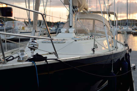 Elegant and modern sailboats moored to a pier in a yacht marina at sunset. Dramatic clouds. Inner...