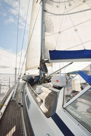 Sloop rigged modern yacht with wooden teak deck sailing near the rocky lake shores. Scotland, UK....
