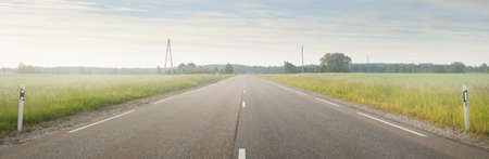 Country highway (asphalt road) through the field and forest at sunrise. Soft sunlight, glowing clouds. Vacations, logistics, remote places. View from the carの写真素材
