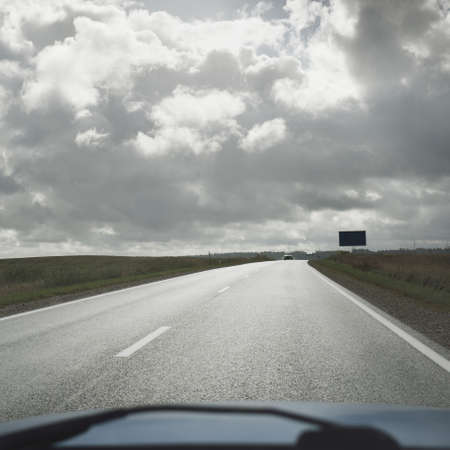 Country highway (asphalt road) through the fields and forest. View from the car. Dramatic storm...