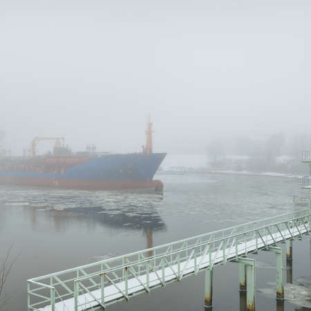 Frozen river, large cargo ship, swing bridge. Snow, thick fog. Concept winter urban landscape....