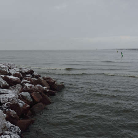 Panoramic view of Baltic sea from sandy shore. Promenade to the lighthouse, breakwaters. Thick white...