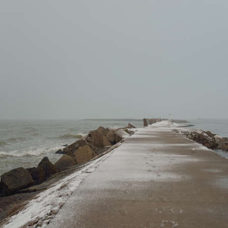 Panoramic view of Baltic sea from sandy shore. Promenade to the lighthouse, breakwaters. Thick white...