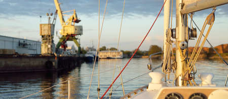 White yacht arriving in port at sunset. Close-up view from the deck to the bow and sails. Dramatic...
