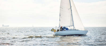 White sloop rigged yacht sailing in an open sea. Clear sky, cloudscape. A view from the sailboat....