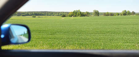 Driving a car through the green country fields and forest on a sunny day. Clear blue sky. Idyllic rural scene, concept landscape. Nature, remote places, logistics, summer vacations, road tripの写真素材