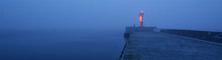 Panoramic view of Baltic sea. Port entrance, lighthouse, breakwaters. Thick fog, mist, blue light. Waves, water splashes, long exposure. Seascape. Monochrome scenery. Danger, safety conceptsの写真素材