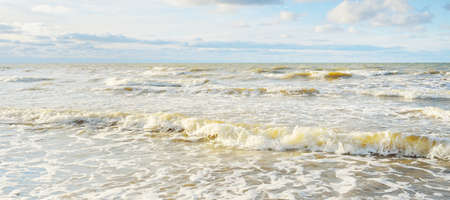 Panoramic view of the Baltic sea from a sandy shore (sand dunes). Clear sky with glowing clouds, waves and water splashes. Idyllic seascape. Warm winter weather, climate change, natureの写真素材