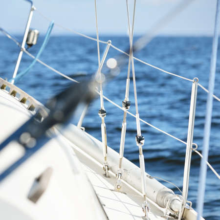 White sloop rigged yacht sailing in the Baltic sea at sunset. View from a cockpit. Boat side railing...