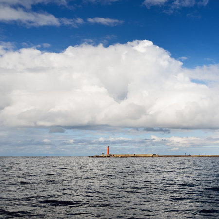Baltic sea at sunset. Dramatic blue sky after the storm, ornamental cumulus clouds. Lighthouse in...