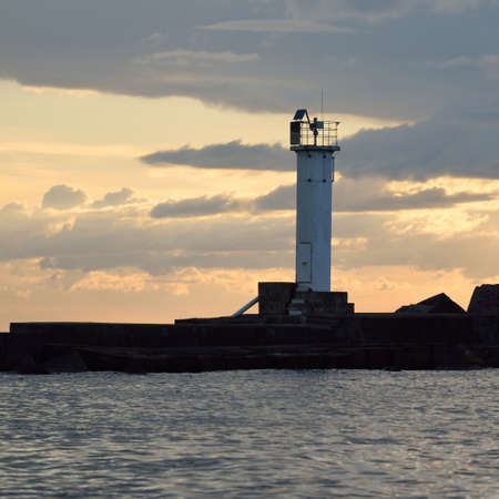 Lighthouse with a solar battery. Baltic sea. Dramatic sunset sky after the storm. Glowing clouds,...