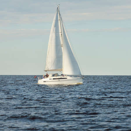 Sloop rigged yacht sailing in the Baltic sea. Sunset. Dramatic sky after the storm, soft sunlight. Transportation, travel, cruise, yachts racing, sport, recreation, leisure activity, lifestyle, familyの写真素材