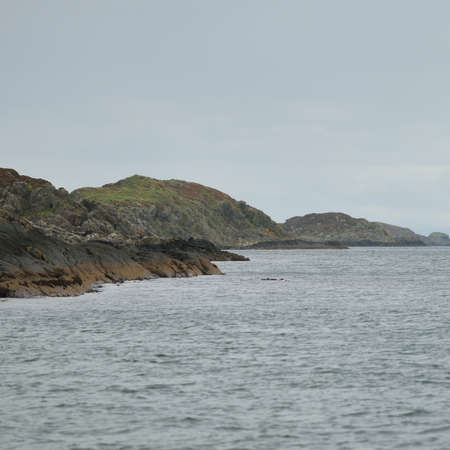 Rocky lake shore, mountain peaks, mountains, valleys and hills. Panoramic view from a sailboat. Dramatic sky. Scotland, UK. Atmospheric landscape. Travel destinations, landmarks, hiking, ecotourismの写真素材