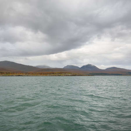 Rocky lake shore, mountain peaks, mountains, valleys and hills. Panoramic view from a sailboat....