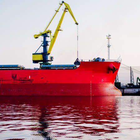Large cargo ship loading in port terminal, cranes in the background. Freight transportation, nautical vessel, logistics, global communications, worldwide shipping, economy, business, industryの写真素材