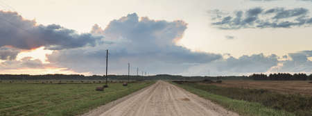 An empty country road through the agricultural fields and forest during the storm. Dramatic sky,...