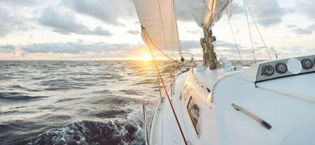 Yacht sailing in an open sea at sunset. Close-up view of the deck, mast and sails. Clear sky after...