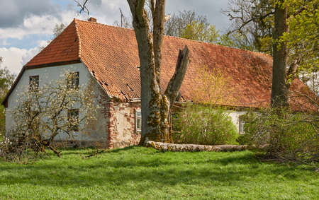 An old stone house. Red tile roof, wooden details. Green garden. Spring, early summer. Idyllic rural scene. Architecture, exterior design, building traditions, countryside living, tourism themesの写真素材