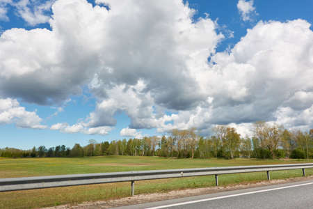 An empty highway (new asphalt road) through the field and forest. Dramatic storm clouds before the rain. Tourism, road trip, freedom, vacations, logistics, remote places conceptsの写真素材